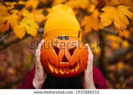 Girl holding jack-o-lantern in front of face. Carved halloween spooky pumpkin. Gold autumn colors.