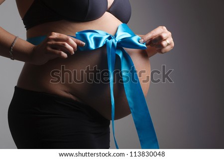pregnant woman with a big belly ties a blue ribbon around her belly
