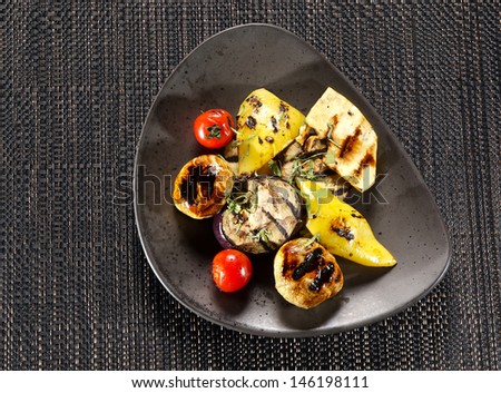 Grilled vegetables. Plate of grilled vegetables with arugula salad on a black background