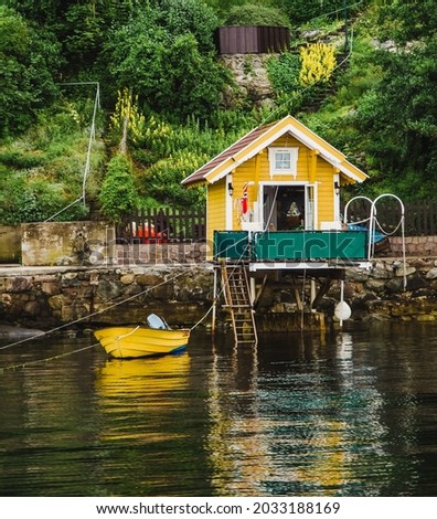 Small yellow colorful house and wharf with moored boat in Oslo fjord in Norway. Oslo fjord shore and classical scandinavian tiny wooden houses