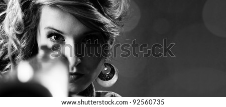 Attractive girl pointing a gun over black background. Closeup portrait. black&white