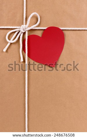 Blank red valentine card or gift tag on a brown paper package background tied with string.  Space for copy.