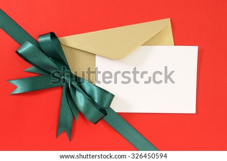 Christmas or birthday card with envelope, red gift paper background, diagonal green ribbon bow, copy space
