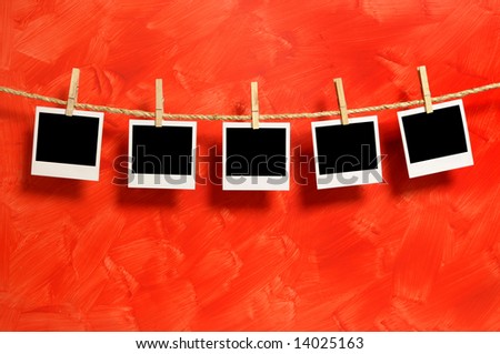 Several blank polaroid style instant camera photo prints hanging on a rope or washing line isolated against a red background.  Space for copy.