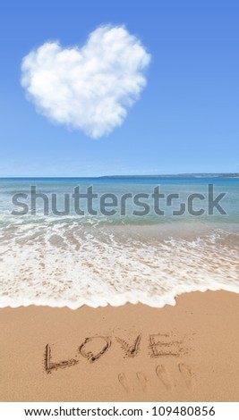 Love text drawn on the beach shore with the blue sky and heart shape cloud in the background. Love Concept.