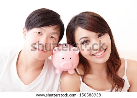 young happy couple lying in a bed with pink piggy bank, asian family