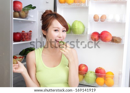 Healthy Eating Concept .Diet. Beautiful Young Woman eat kiwi fruit near the Refrigerator with healthy food. Fruits and Vegetables, asian model