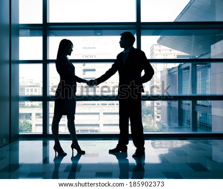 successful business woman and man handshaking with office building