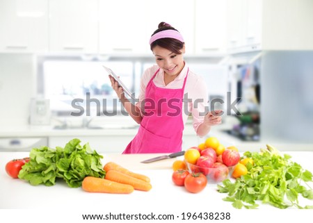 Young woman wearing kitchen apron with digital tablet in kitchen with fresh produce vegetables preparing for a healthy meal, asian