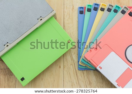 Stack of colorful floppy disks and a floppy disk drive on a wooden table