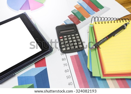 Calculator on top of pile of colorful graph chart paper on desk with yellow notepad, pencil and tablet computer. business concept of financial analysis