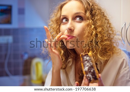 Funny young woman eating sweet cake in the kitchen at night