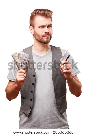 Handsome man in doubt with banking card and cash in his hands isolated on white background.