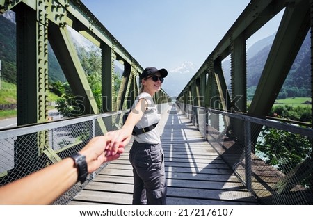 Traveling together. Follow me. Young woman holding boyfriend's hand walking on mountain river bridge. Stok fotoğraf © 