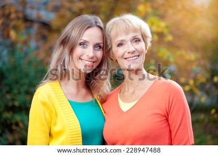 Portrait Of Middle aged Mother And her Adult Daughter smiling at camera outdoors