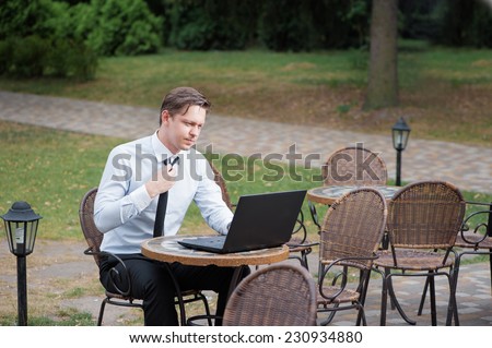 Hard working businessman. Attractive young tired man in formal shirt and tie working on laptop while sitting at the table outdoors