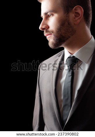 Serious and stylish. Thoughtful young bearded man in suit and tie standing against black background