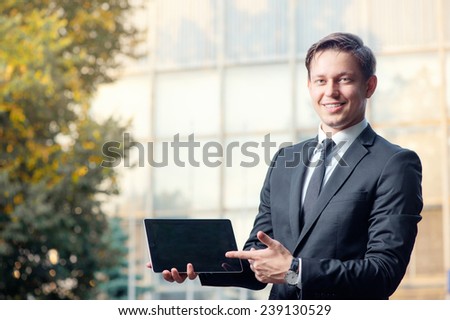 Join a digital age. Cheerful young caucasian man in formal wear showing a screen of digital tablet and smiling at camera