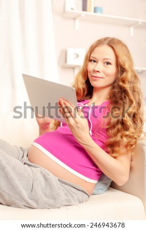 Pregnant woman with tablet. Beautiful pregnant caucasian woman using digital tablet while lying on a couch