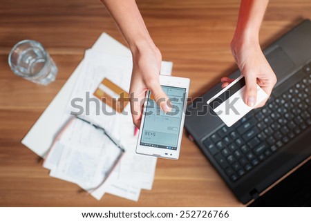 Business work place with female hands holding smart phone and bank card, top view