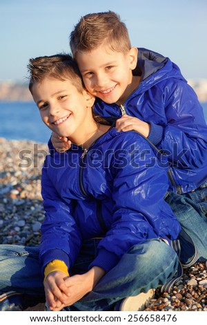 Family happiness. Two little smiling children boys brothers playing and hugging on the beach looking at camera.