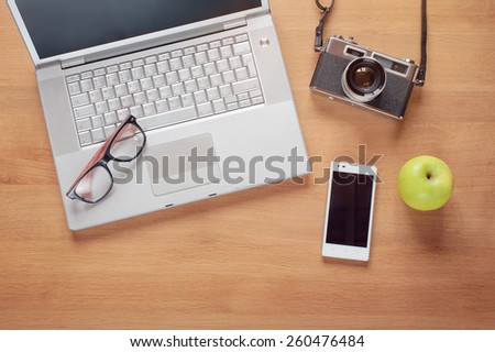 Overhead of modern comfort work place. Different objects on wooden background. Items include camera, glasses, laptop, smartphone and apple