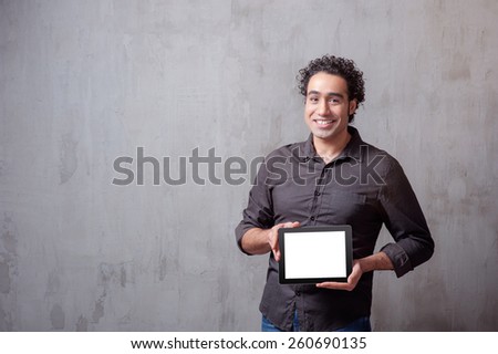 Copy space on his tablet. Cheerful young man holding a digital tablet and smiling while standing against grey background