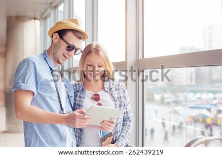 Digital technology and traveling. Young loving couple in casual wear using tablet computer while standig in the airport terminal waiting for boarding.