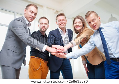 Team of winners. Partnership and creative work. Group of business people holding their hands together and smiling while standing on office. Focus on hands.