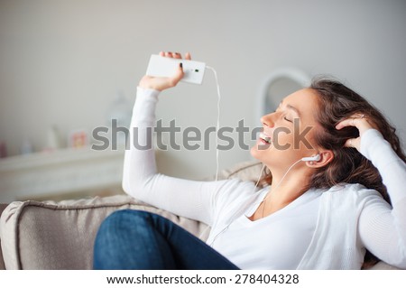 Relax in the rhythm of my music. Attractive young woman lwith earphones and smartphone sitting on sofa at home.