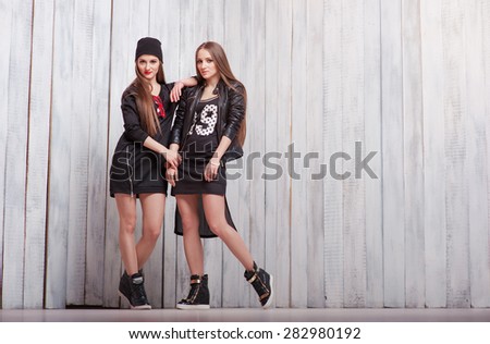 Youth and urban fashion. Attractive twins sisters. Two beautiful smiling young women standing together.