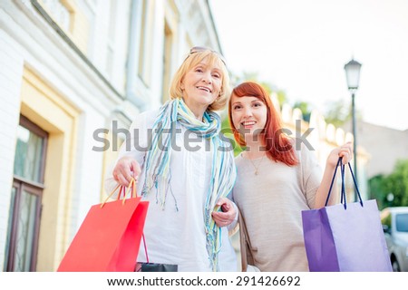 Holiday with mother. Family shopping. Outdoor portrait of smiling caucasian middle aged woman and her adult daughter holding bags.