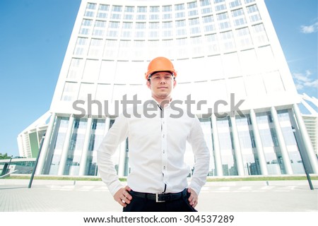Confident contractor. Serious young man in shirt and hardhat smiling while standing outdoors
