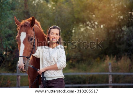 Portrait of young smiling beautiful woman walking with brown horse outdoors