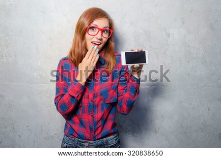 Your text here. Amazed young woman in plaid shirt showing smartphone screen with copy space on it.