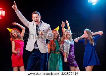 Carnival and party. Emcee with microphone. Group of cheerful friends dancing in nightclub.