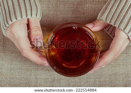 Female hands in the sleeves with a cup of black tea