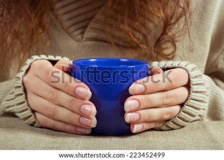 Female hand in a long-sleeved sweater, holding a blue cup