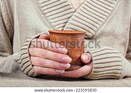 Female hand in a long-sleeved sweater with a clay cup