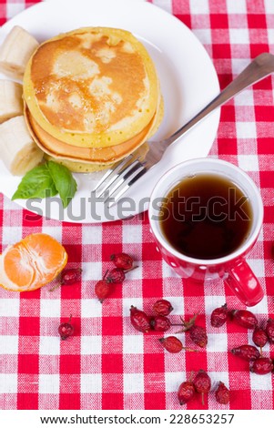 The composition of the plates with pancakes, tea cups and hips. National American dish - pancakes. Pancakes on a plate with banana and mint leaves. A hearty breakfast