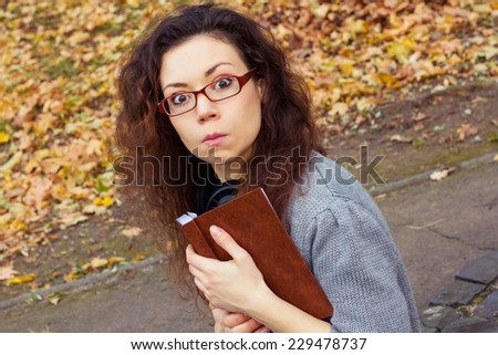 Funny girl in glasses with a book in the park. Girl grimaces. Girl with the book in autumn park