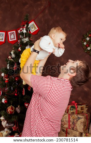 Father with a baby near Christmas tree. Concept of happy childhood. Celebrating Christmas in a homely atmosphere. Father dabbles with the child, laughing merrily.Merry Christmas. Family celebration.