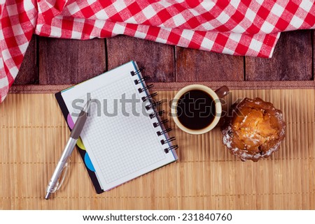 Cup of coffee and cake on the table next to the notepad. The idea of freelance work, starting a new business, the lunch break. Notepad with pen on a wooden table. Still on the kitchen table.
