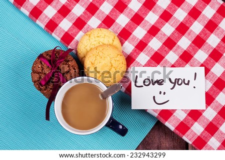 A cup of coffee on the table next to cookies. Surprise your loved one with a note, \