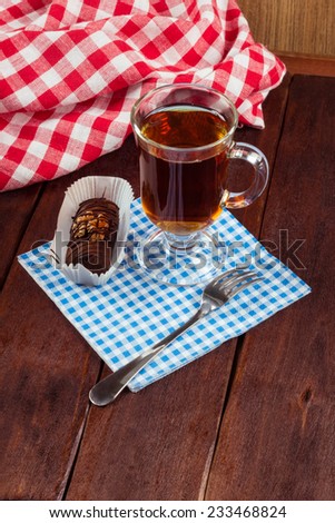 Cup of strong black tea on a table next to the cake. Cup of tea with dessert and fork on a wooden table in the cafeteria.