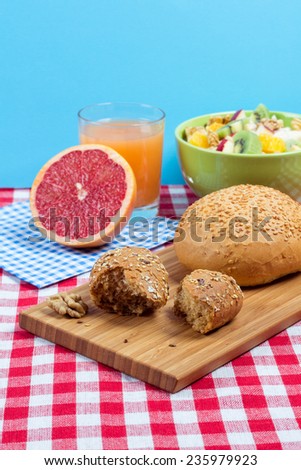 Bread with bran and sunflower seeds on a wooden board. Delicious fruit dinner for vegetarians. Fruit salad and a glass of fresh juice on the table.