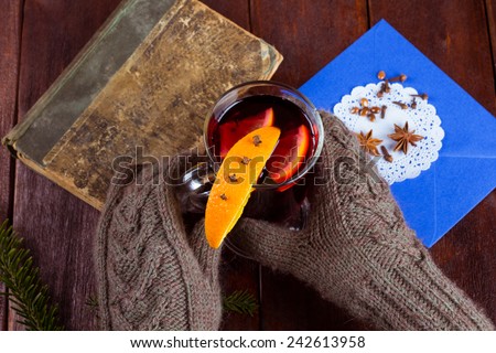 Warm knitted mittens and a glass of hot mulled wine. Orange slice, spice, old book, gloves, coniferous branch on the table. Mulled wine to warm up in winter.