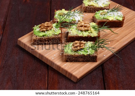 Canapes with paste of avocado, walnuts, cheese and sesame seeds. Snack of canapes with avocado, nuts and herbs on a kitchen board. The concept of the restaurant, a healthy diet food, holiday food.