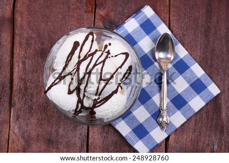 A serving of vanilla ice cream with chocolate icing. Top view. Bowl of ice cream, spoon and napkin. Ice cream on the kitchen table. Serving dishes in the cafeteria or restaurant. Sweet dessert.