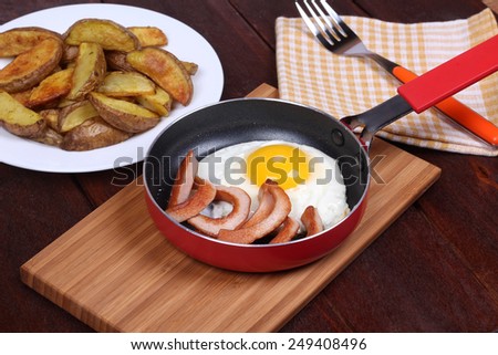 Classic hearty lunch. German cuisine. International cuisine. Calorie fried food. Frying pan with fried egg and sausages near the plate with baked potatoes. Top view.